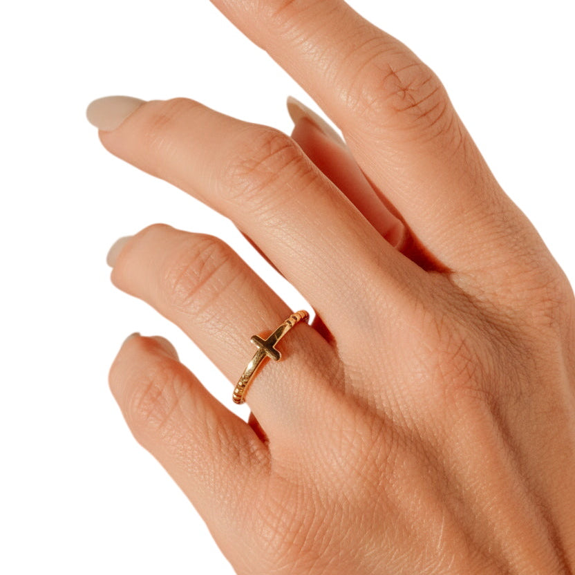 Hand wearing a gold ring with a neutral background
