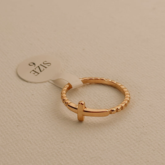 Gold ring with a cross design on a beige background