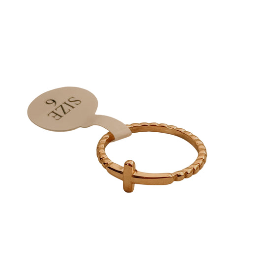 Gold ring with a cross design on a beige background